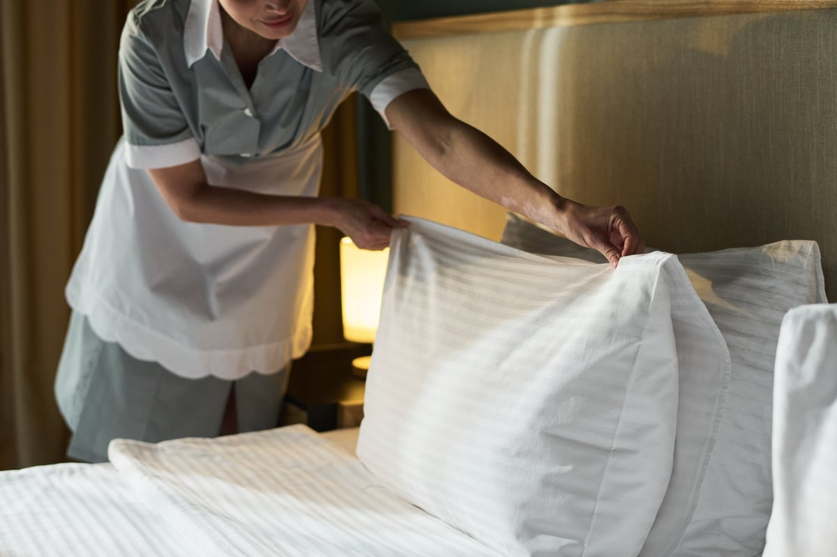 Housekeeper smoothing sheets and arranging pillows on a bed